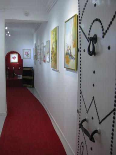 Couloir avec tapis rouge, portes décorées et peintures accrochées aux murs.